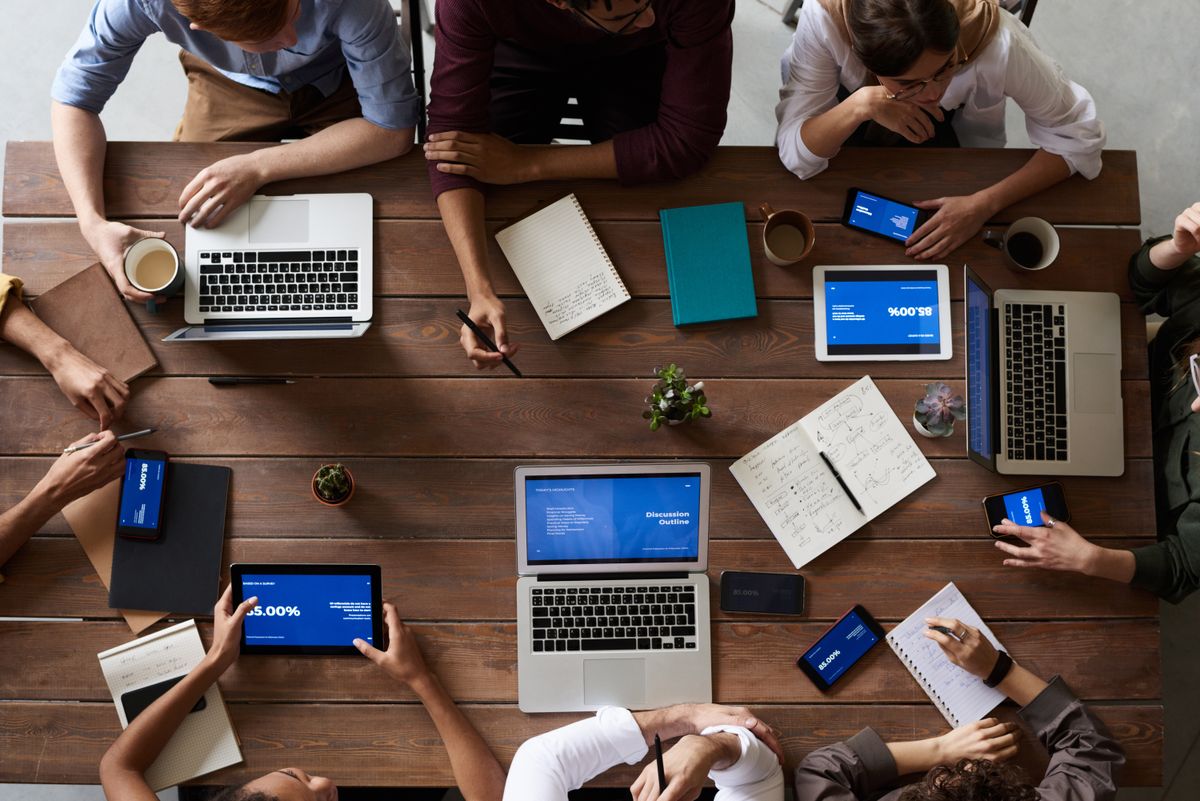 Team vergleicht am Besprechungstisch Strategien auf Laptops und Tablets